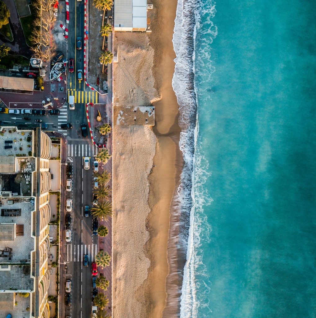 A photo of the beach at Cannes taken from above with the sea on the right-hand side and the city and roads on the left